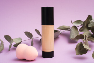 A face foundation cream and sponge next to a eucalyptus branch. The concept of natural makeup, the...