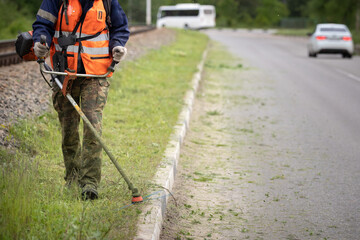Closeup of a man with a lawn mower in his hands. A worker mows the grass on the side of the road. Improvement of the adjacent territory - 428669053