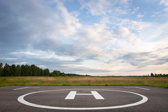 A large area with a special symbol in the center for helicopter landing. Private helipad in a green field against the backdrop of evening clouds.
