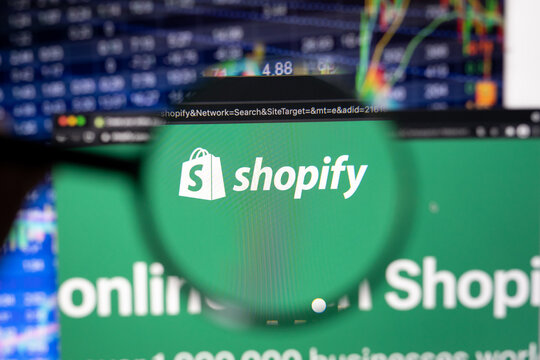Shopify company logo on a website with blurry stock market developments in the background, seen on a computer screen through a magnifying glass