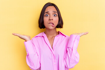 Young mixed race woman isolated on yellow background confused and doubtful shrugging shoulders to...