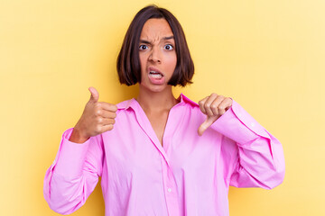 Young mixed race woman isolated on yellow background showing thumbs up and thumbs down, difficult...