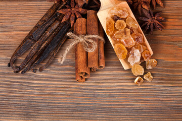 Vanilla beans, cinnamon sticks, crystals of brown sugar and star anise on a wooden background. Top view. Sweet spices concept.
