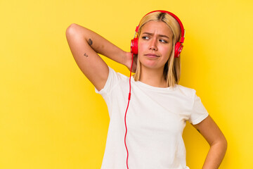 Young venezuelan woman listening music isolated on yellow background touching back of head, thinking and making a choice.