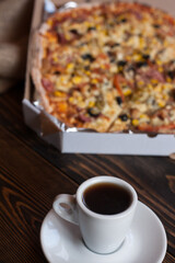 A mug of aromatic coffee and delicious homemade pizza with corn, meat, tomatoes, mushrooms and cheese. Pizza up close. 