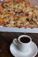 A mug of aromatic coffee and delicious homemade pizza with corn, meat, tomatoes, mushrooms and cheese. Pizza up close. 