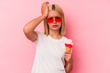 Young venezuelan woman eating an ice cream isolated on pink background being shocked, she has remembered important meeting.