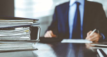 Binders with papers are waiting to be processed by man accountant in blue blazer staying at home...