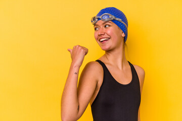 Young swimmer venezuelan woman isolated on yellow background points with thumb finger away, laughing and carefree.