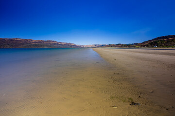 Long exposure photograph, Sandy Spit, blue water, in the distance you can see a mountain range with small houses.
