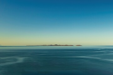 Fototapeta na wymiar Long exposure photograph, blue water blue sky, small island in the distance, minimalism.