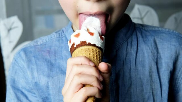 child, a boy of 7 years old holds a waffle cone with delicious popsicles in his hand, poured with sweet syrup and eats it, the concept of a happy childhood, impressions, limiting sweets and sugar