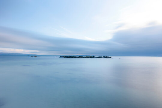 Horizontal photo long exposure, sea blue horizon in the distance a small island can be seen, blue sky