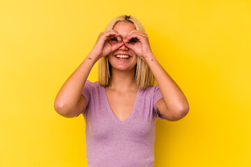 Young venezuelan woman isolated on yellow background showing okay sign over eyes