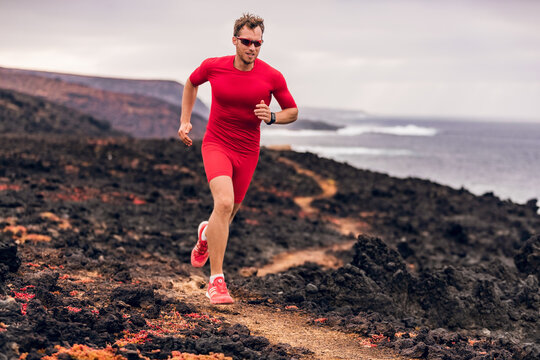 Mountain running ultra runner man athlete training cardio outdoor in extreme conditions on volcanic trail in coast landscape. Wet red rocks. Sports athlete wearing compression clothes and shoes.