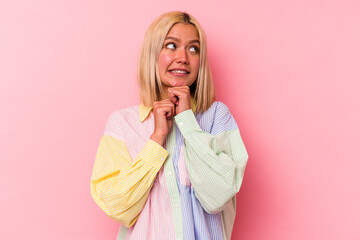 Young venezuelan woman isolated on pink background keeps hands under chin, is looking happily aside.