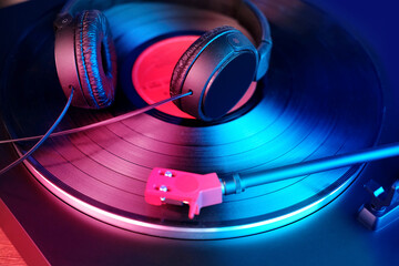 close-up of a pickup head, black headphones on a vinyl record, colored lights, analogue retro music concept, audio experience, relaxation, musical enjoyment, vintage technology © kittyfly