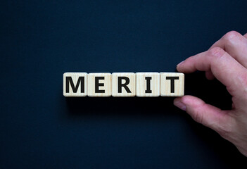 Merit symbol. Wooden cubes with the word 'merit'. Businessman hand. Beautiful black background,...