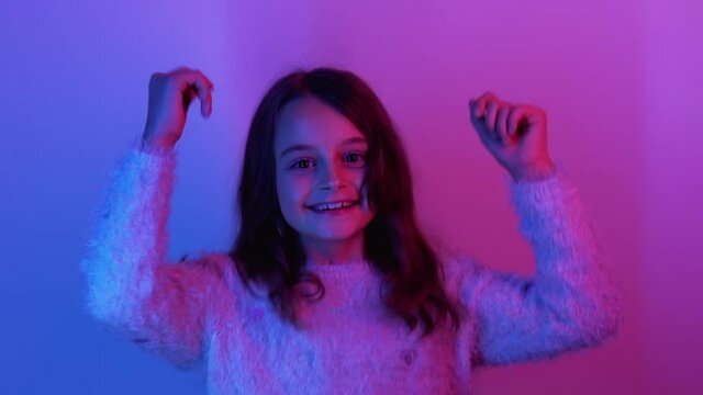 Happy kid. Fun childhood. Positive lifestyle. Excited joyful amused little cute girl enjoying jumping dancing smiling in pink blue neon light on bright background.