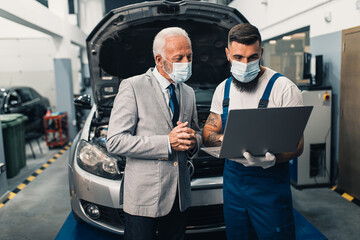 Car mechanic talking with senior business man costumer during periodic car condition check. They...