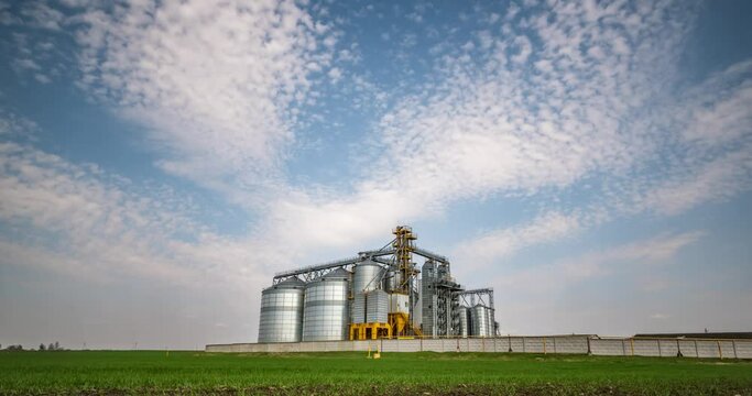 Time lapse of modern granary elevator against the blue sky. Silver silos on agro-processing and manufacturing plant for processing drying cleaning and storage of agricultural products.