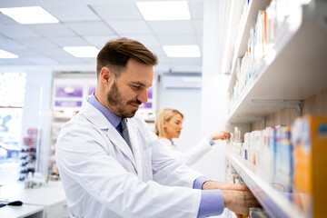 Caucasian male pharmacist working in drug store arranging medicines.