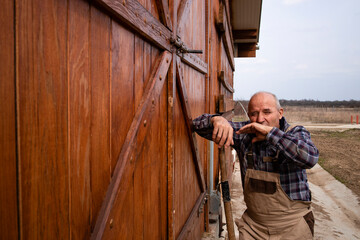 Tired farm worker standing by the wooden farmhouse doors and yawning.