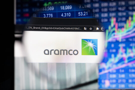 Aramco company logo on a website with blurry stock market developments in the background, seen on a computer screen through a magnifying glass