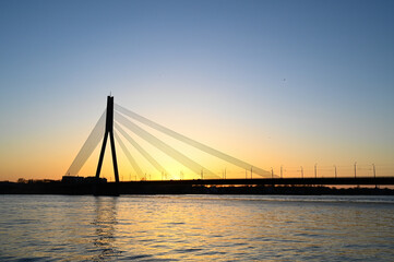 Fototapeta na wymiar Scenic view of long cable-stayed bridge silhouette over the river at sunset.