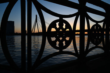 View of cable-stayed bridge silhouette over the river at sunset through the railings with unique ornaments.