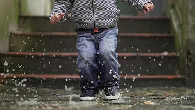 Child jumping into puddle in slow-motion. Toddler jumps into water