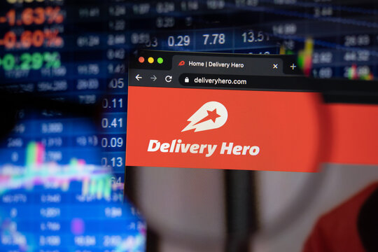 Delivery Hero company logo on a website with blurry stock market developments in the background, seen on a computer screen through a magnifying glass