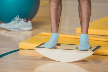Male trainer seen using a wooden balance board. Different balance sports equipment is seen around...