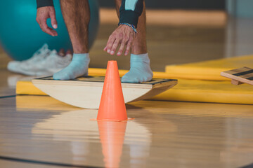 Male trainer seen Touching a cone while on wooden balance board. Different balance sports equipment...