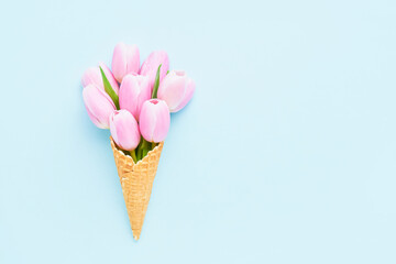 Pink tulips bouquet in waffle ice cream cone on a blue background. Mothers Day, Valentines Day, bachelorette concept.