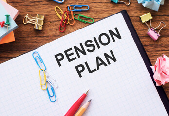 Notepad with the text PENSION PLAN on the table with colored paper clips and crumpled sheets.