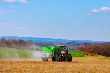 Fotobehang The tractor spreads granular fertilizer on a grass field. Agricultural work. Nitrate. Mineral fertilizers. © Yaroslav