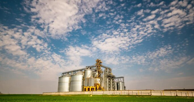 Time lapse of modern granary elevator against the blue sky. Silver silos on agro-processing and manufacturing plant for processing drying cleaning and storage of agricultural products.