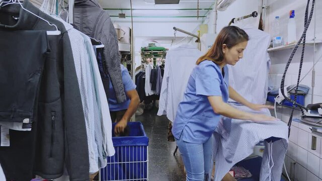 Female laundry worker ironing clean clothes in dry cleaning salon