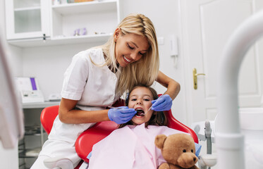 Cute little girl sitting on dental chair and having dental treatment.