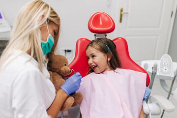 Cute little girl sitting on dental chair and having dental treatment.