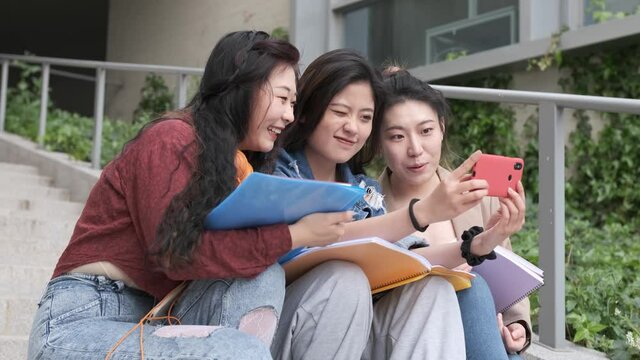 Asian college students taking a selfie with a mobile phone outside the university campus. Education concept.