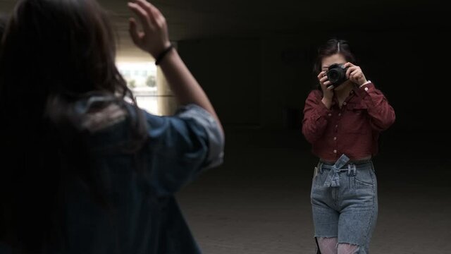Young asian woman photographer taking a photo with a professional camera to someone while posing
