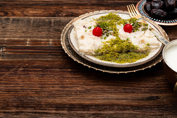 Traditional Turkish milky Ramadan Dessert named Gullac with sugar, powder of pistachio, milk and gullac sheets (rice wafer or rice paper sheets) on vintage metal plate and wooden background.