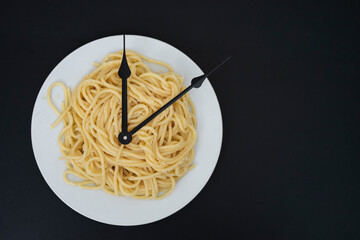 spaghetti on a white plate, on black background, and clock tongues representing boiling time