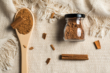 Fototapeta na wymiar Ground cinnamon and sticks on a rustic fabric or tablecloth and cinnamon powder in a tiny glass jar. Flat lay, healthy life and ayurveda concept.