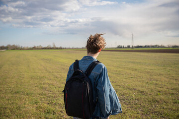 young traveler boy with backpack on his back looks at an empty field. Travel concept