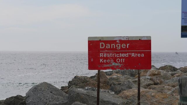 This video shows a "danger restricted area" sign posted near rocky ocean waters, warning visitors to stay off.