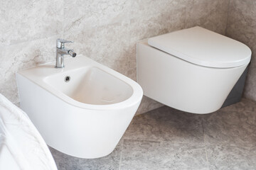 White wall-hung bidet and toilet on gray ceramic tiles in bathroom - obrazy, fototapety, plakaty