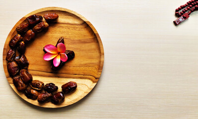 Ramadan background, dates heart shaped on a wooden plate and prayer beads on a cream background
